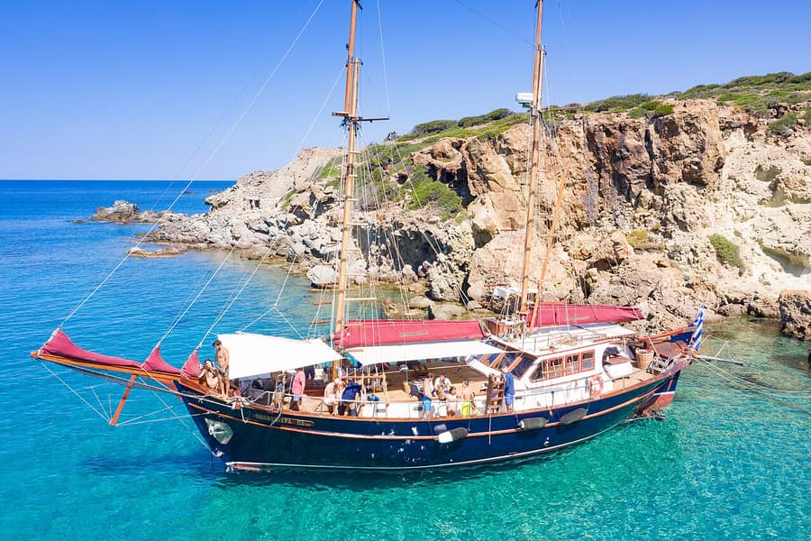 Milos sailing tour: a traditional wooden two-masted sailing boat with guests on deck, anchored in a bay near Kleftiko