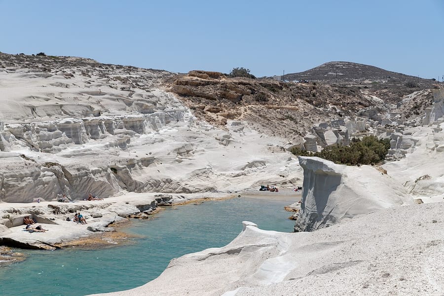 Sarakiniko beach: smooth white volcanic rock around a narrow turquoise inlet, with the open blue sea beyond