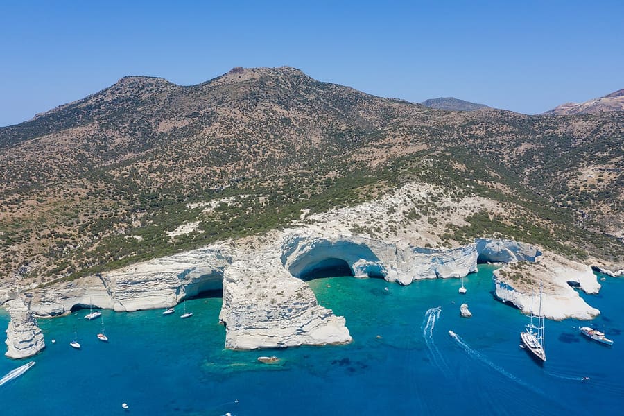 Milos snorkeling cruise: aerial view of the white rock arches and caves of Kleftiko with boats anchored in the blue bay