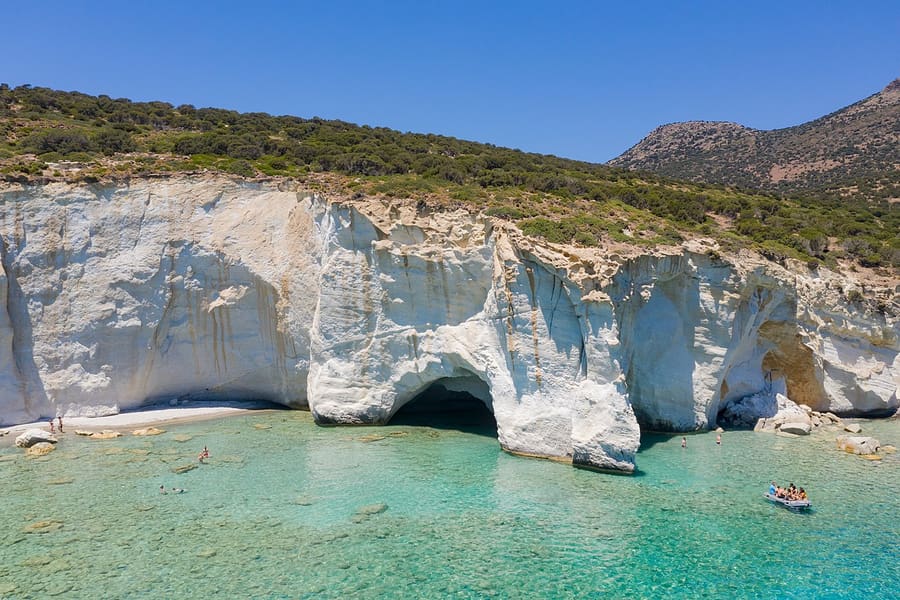 Milos snorkeling cruise: clear turquoise water at the mouths of the white sea caves of Kleftiko, with a small boat near the rocks
