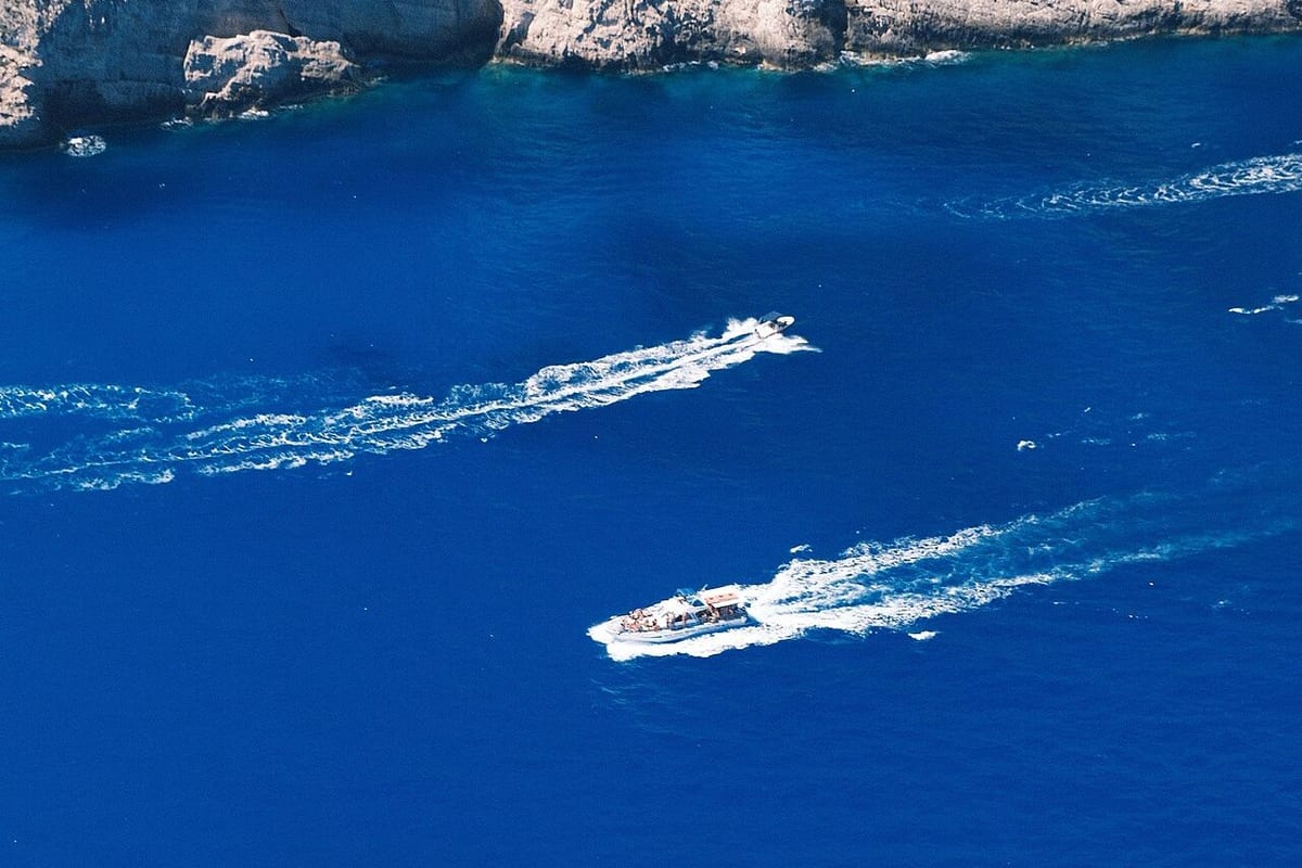 Milos speedboat tour: two speedboats leaving long white wakes on deep blue water below a rocky coast