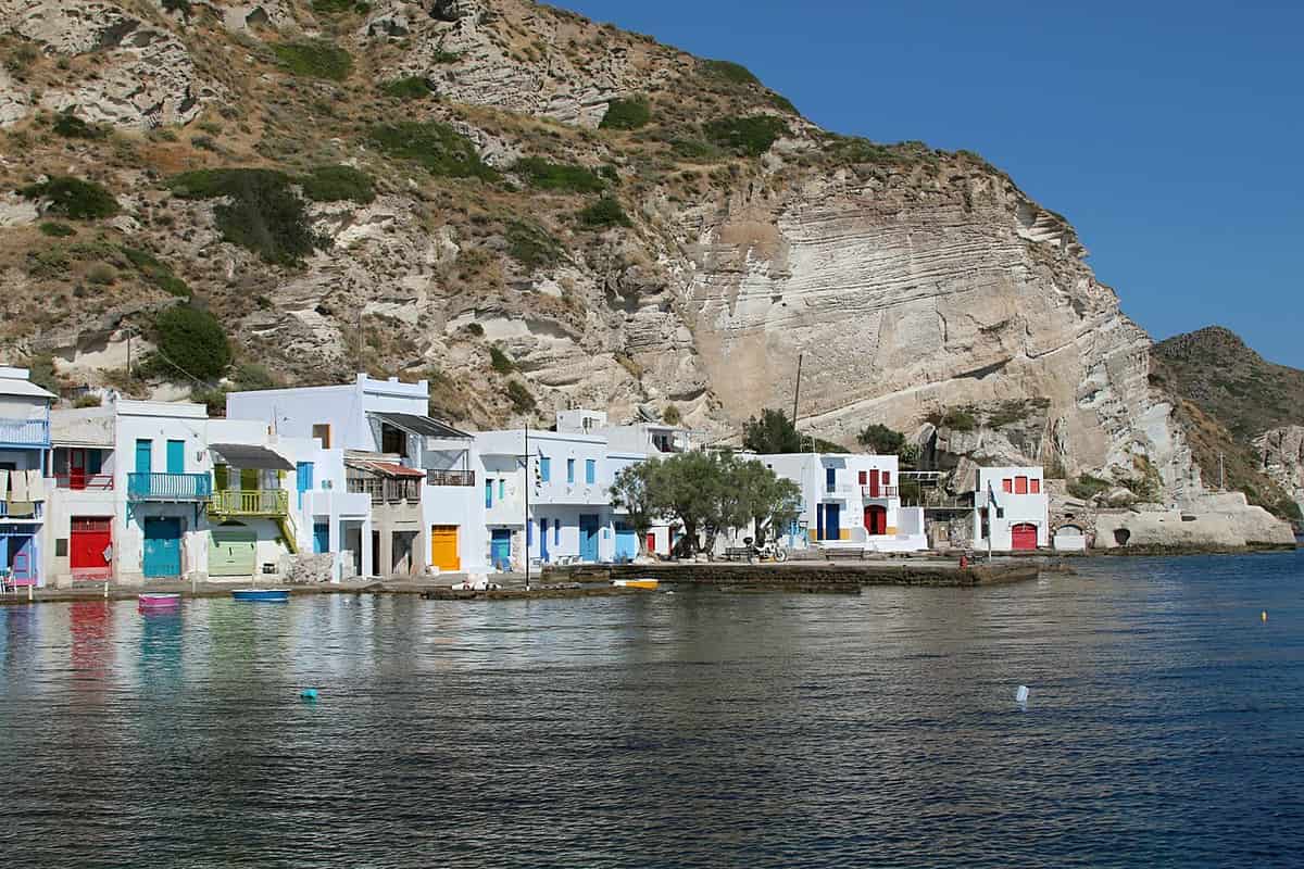 Suites in Milos: white houses with coloured doors at the foot of a pale volcanic rock face on the bay at Klima