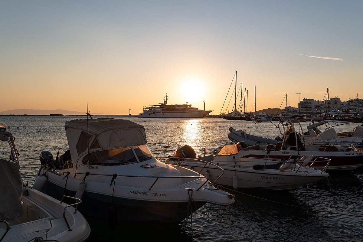 Milos sunset cruise: small motorboats and sailing yachts in a Cyclades harbour as the sun goes down