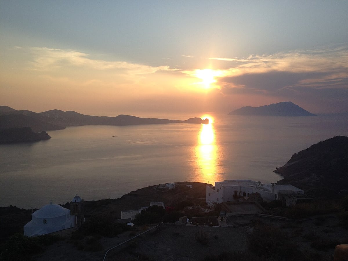 Milos sunset cruise: the sun setting over the sea west of Milos, with islets and a white chapel in the foreground