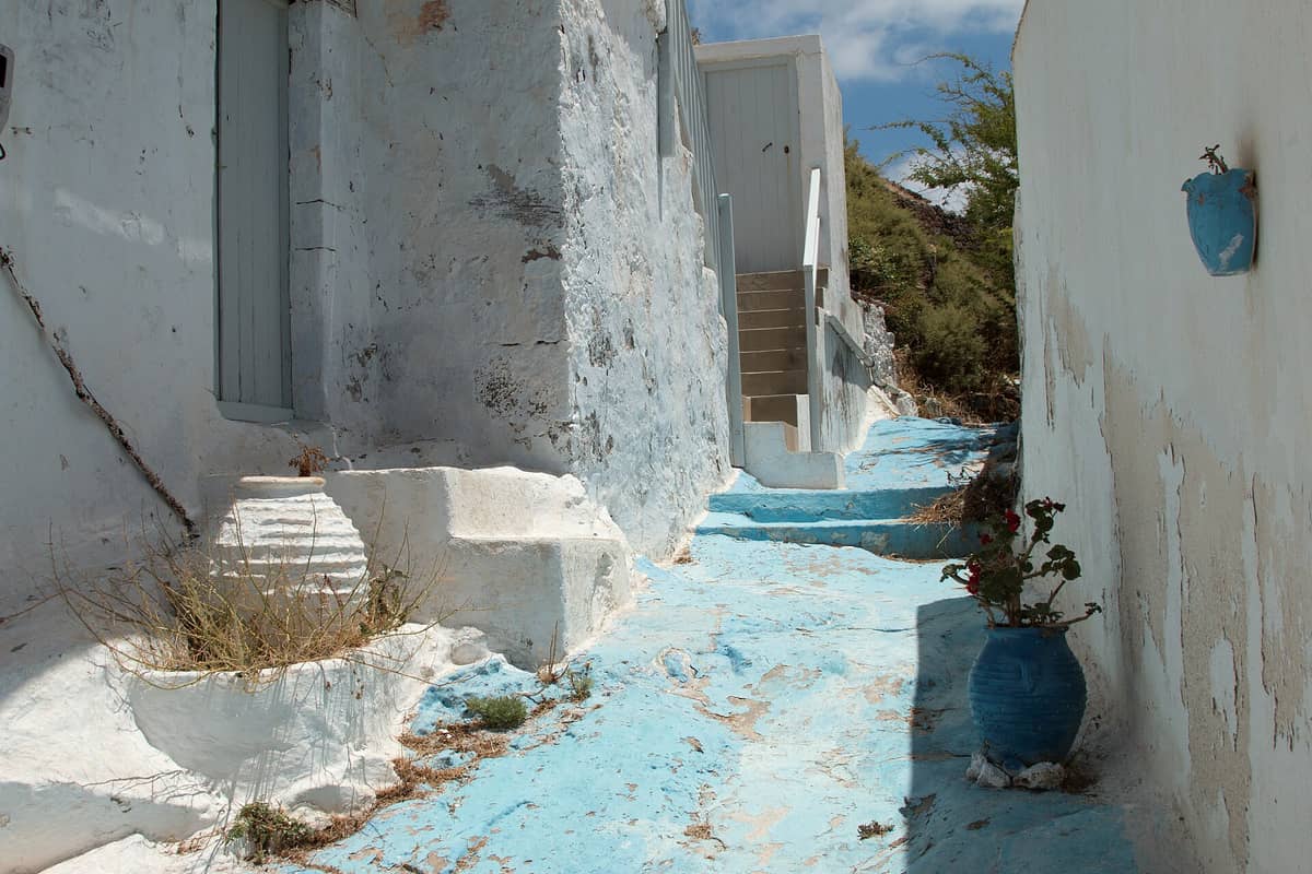 Sweets in Plaka Milos: a whitewashed lane with blue painted steps and flower pots climbing towards the Kastro of Plaka