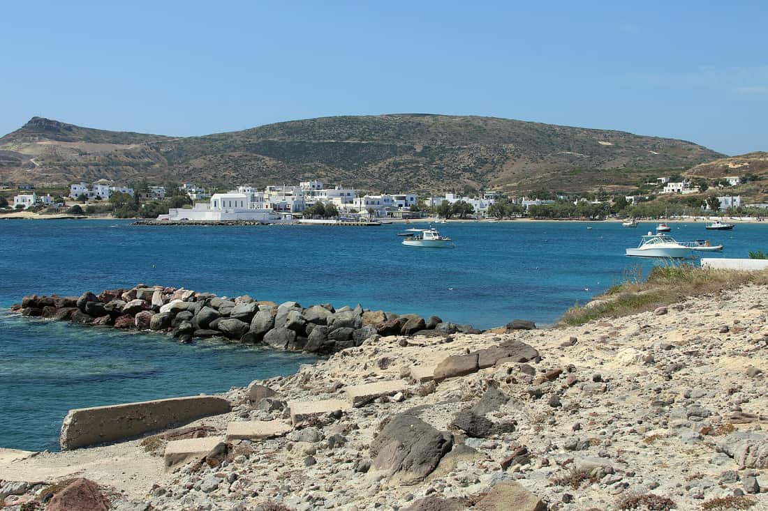 Sweets in Pollonia: the white houses of Pollonia along the bay, with boats on the clear water and the hills of north-east Milos behind
