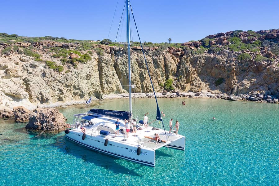 Sykia cave boat tour: a tour catamaran at anchor in a turquoise cove below pale cliffs on the west coast of Milos