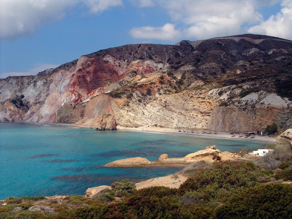 Ηφαίστειο Μήλου: κόκκινα, κίτρινα και λευκά ηφαιστειακά πετρώματα στην ακτή της Φυρίπλακας πάνω από τιρκουάζ νερά