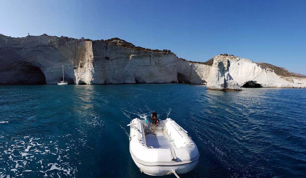 Ιστιοπλοΐα Μήλος: ιστιοπλοϊκό αγκυροβολημένο μπροστά στους λευκούς βράχους και τις σπηλιές του Κλέφτικου, με μια φουσκωτή βάρκα