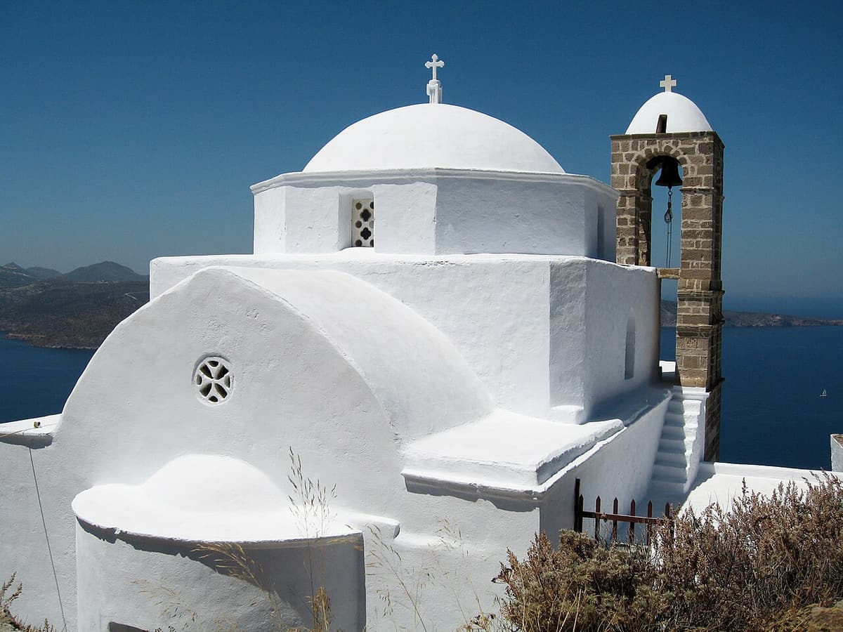 Κάστρο Πλάκας: η λευκή εκκλησία της Παναγίας Θαλασσίτρας με πέτρινο καμπαναριό στην πλαγιά, με την Πλάκα και τον κόλπο της Μήλου πίσω