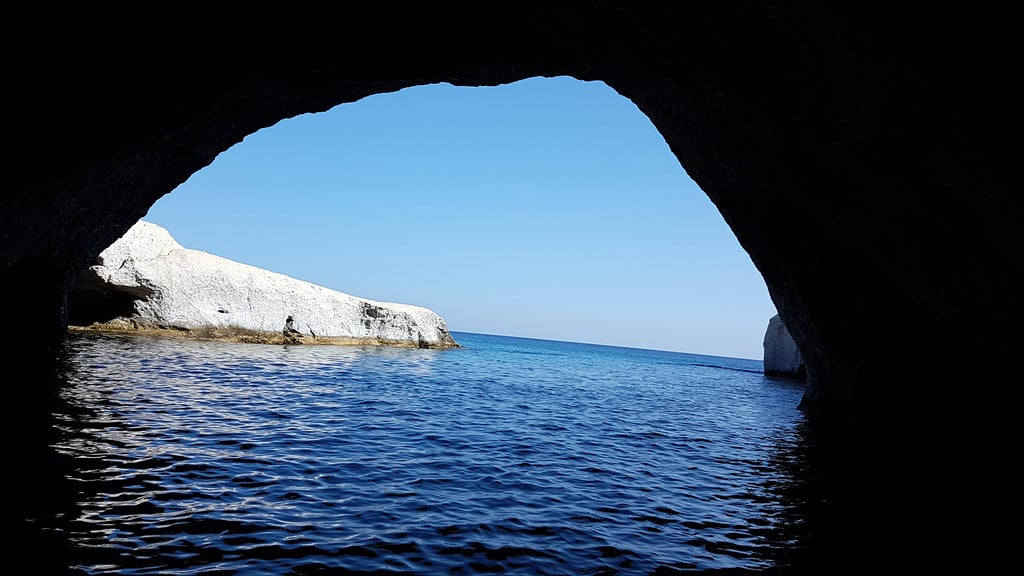 Καταμαράν Μήλος: πέτρινο τόξο σπηλιάς που πλαισιώνει γαλάζια θάλασσα και λευκό βράχο στη δυτική ακτή