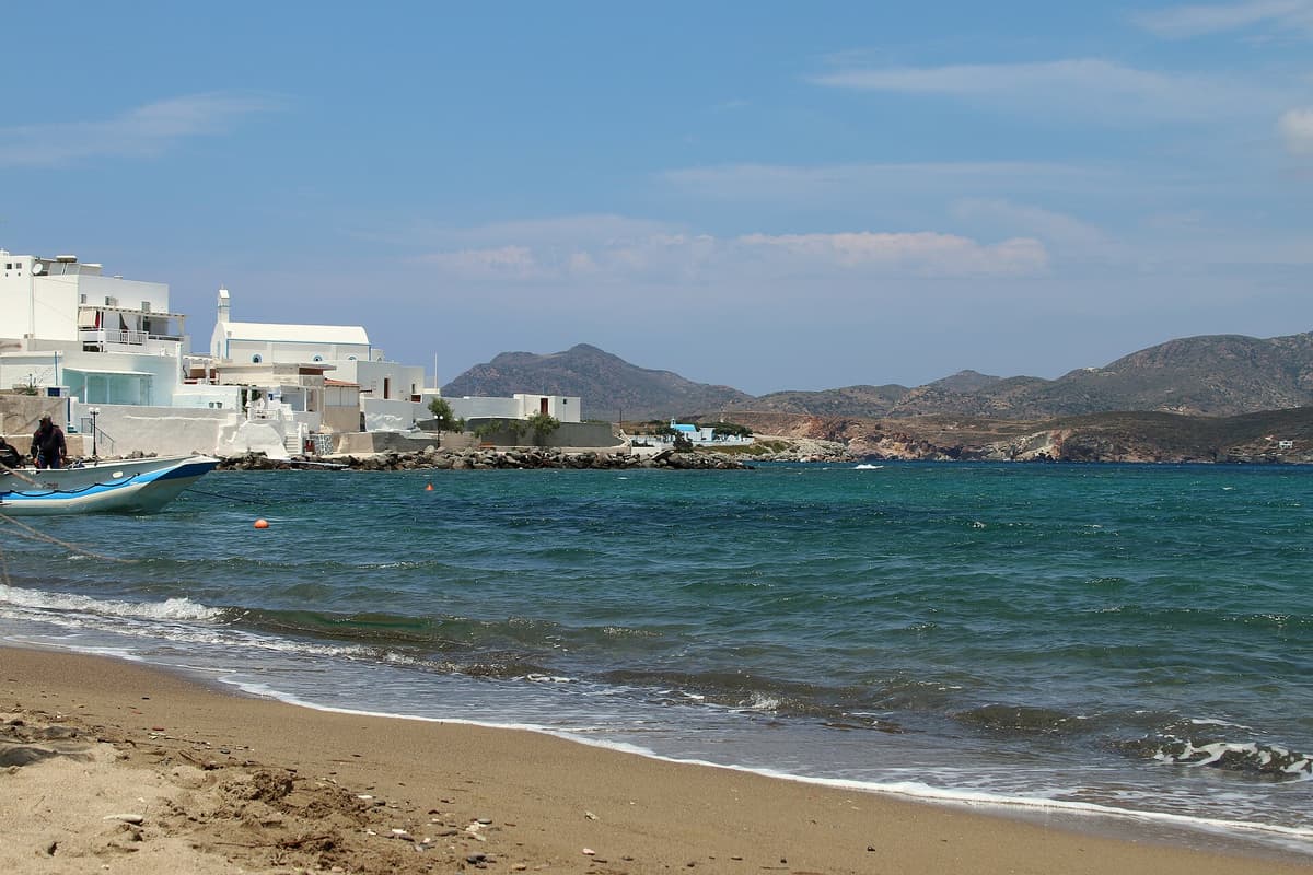 Η αμμουδιά των Πολλωνίων με τα λευκά σπίτια και μια βάρκα στη Μήλο