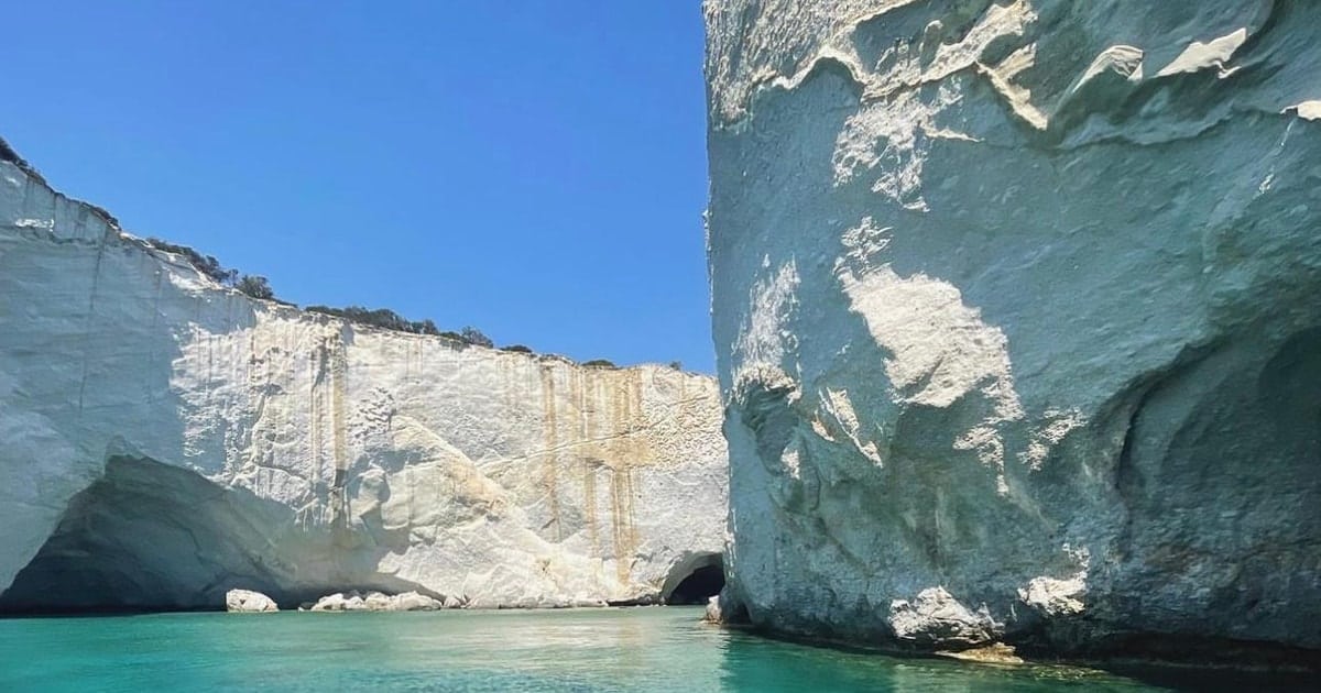 Παραλία Γέροντας: είσοδος θαλάσσιας σπηλιάς σε ψηλό λευκό βράχο, με ήρεμο τιρκουάζ νερό μπροστά