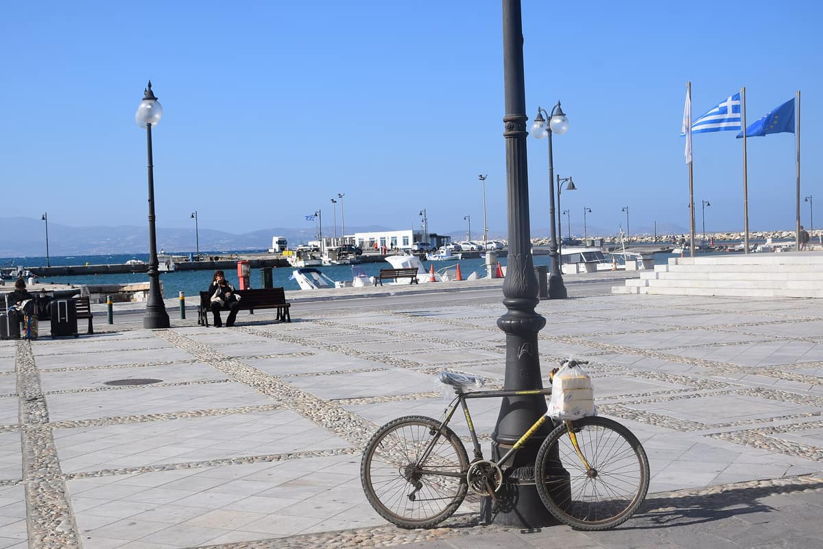 Ποδήλατο δεμένο σε φανοστάτη στην προκυμαία της Νάξου, με το λιμάνι στο βάθος
