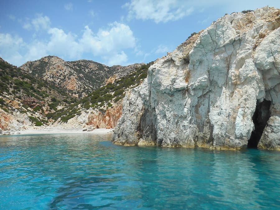 Πολύαιγος: τιρκουάζ νερά μπροστά σε λευκό βράχο με θαλάσσια σπηλιά και ξερές πλαγιές πίσω