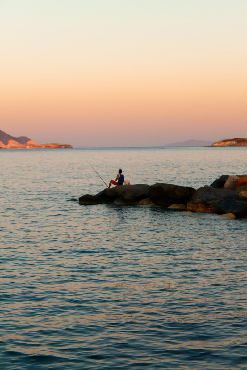 Ψαράς με καλάμι πάνω σε βράχια στη θάλασσα της Μήλου, την ώρα του δειλινού