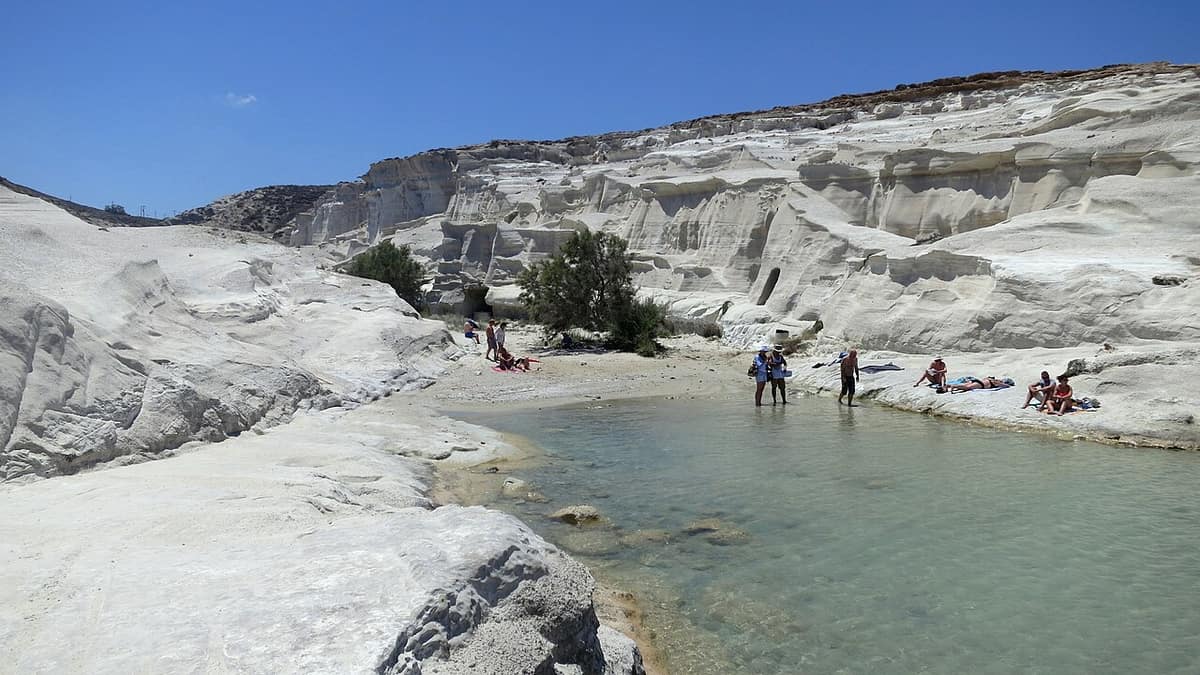 Σαρακήνικο Μήλος: λευκά ηφαιστειακά βράχια γύρω από έναν μικρό κολπίσκο με καθαρό, ρηχό νερό και λουόμενους στην άμμο