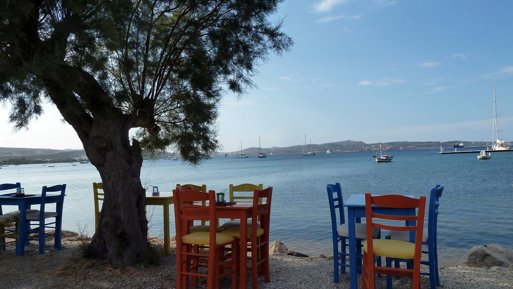 Μήλος τιμές: χρωματιστά τραπέζια και καρέκλες κάτω από αλμυρίκια, δίπλα στη θάλασσα του Αδάμαντα